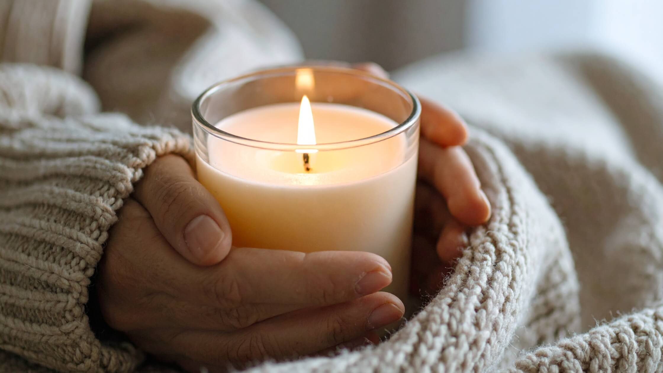 Kerze wird angezündet in dunklem Raum, Hände schützen die Flamme, warmes goldenes Licht, symbolisch für das neugeborene Lichtkind