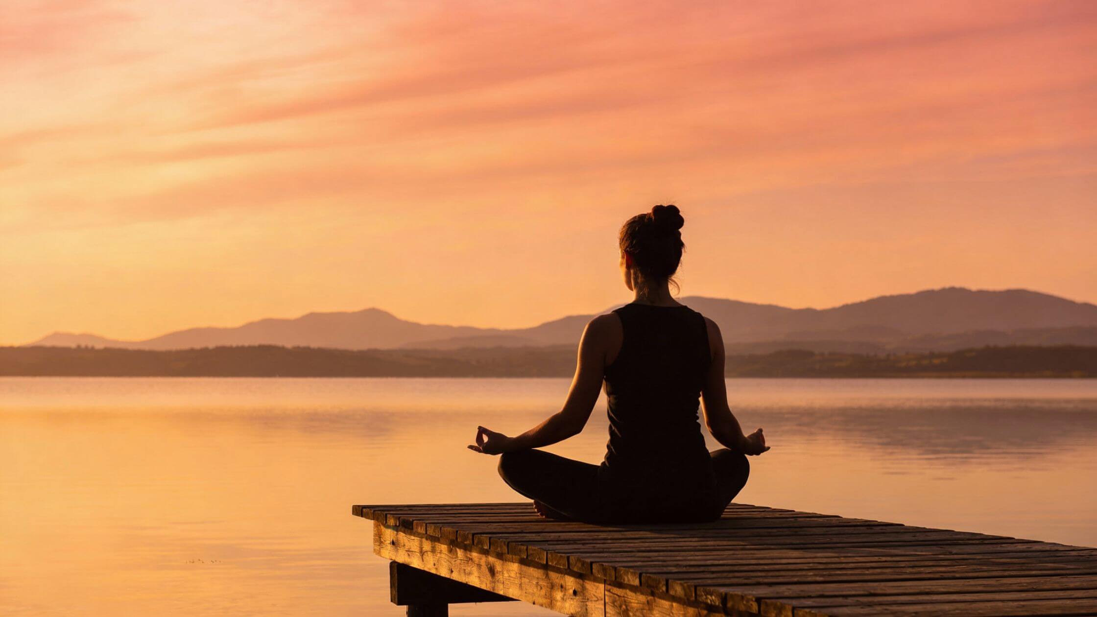 Frau meditiert bei Sonnenuntergang am Wasser, symbolisiert innere Ruhe und spirituelle Transformation durch Energiearbeit