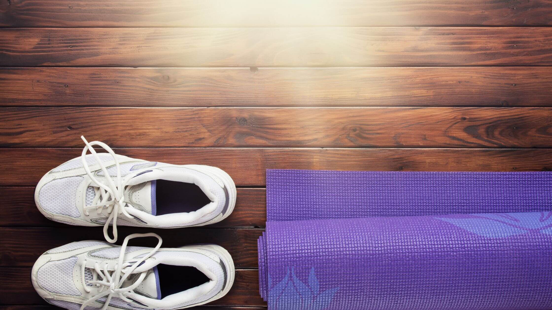 Zusammengerollte Yogamatte und unbenutzte Sportschuhe – symbolisiert das Aufschieben von Sport und Selbstfürsorge
