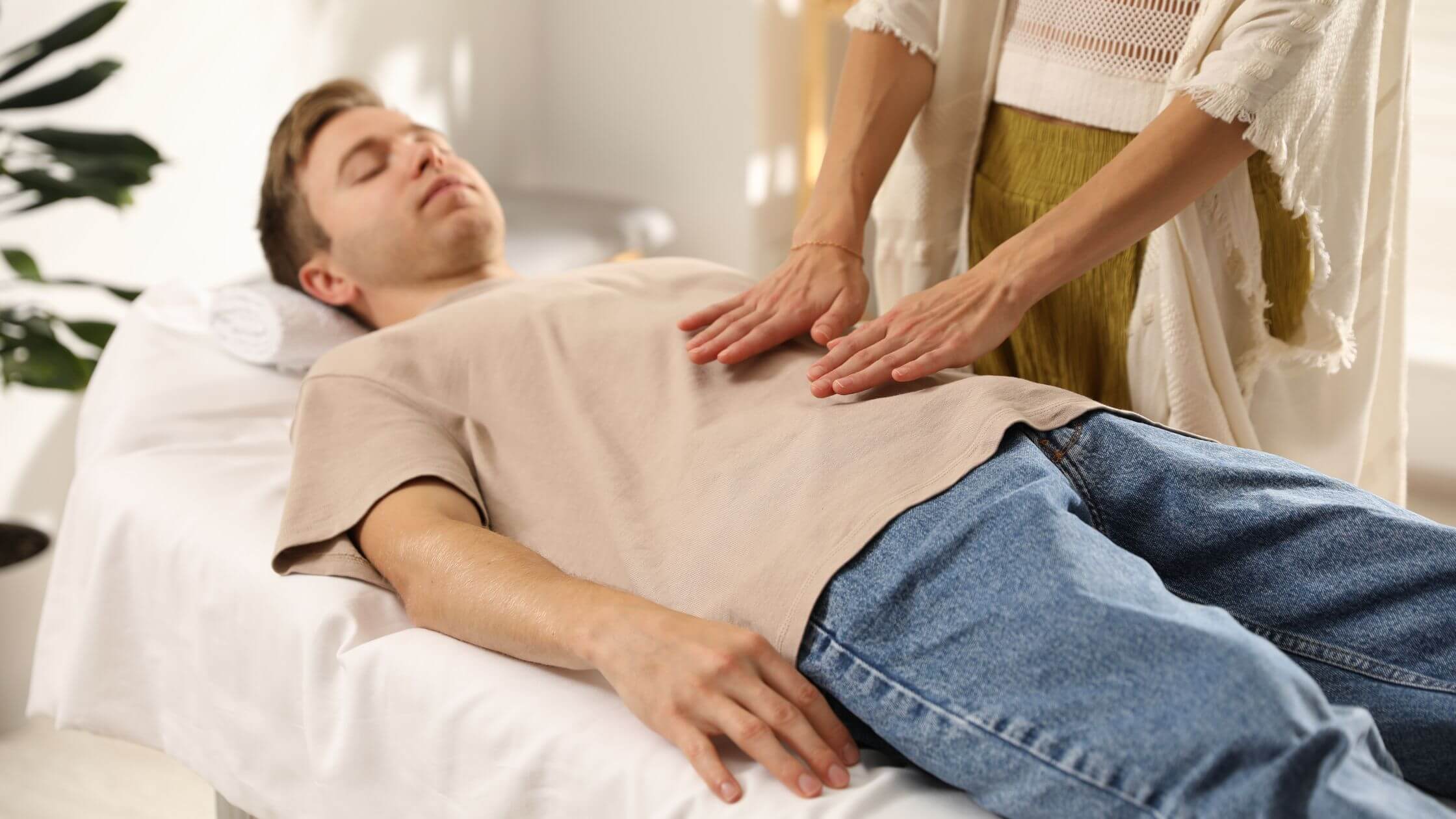 Reiki lernen und verstehen: Der komplette Guide zur universellen Lebensenergie Professionelle Reiki-Behandlung auf Massageliege, Praktizierender legt Hände auf entspannte Person in ruhigem Behandlungsraum