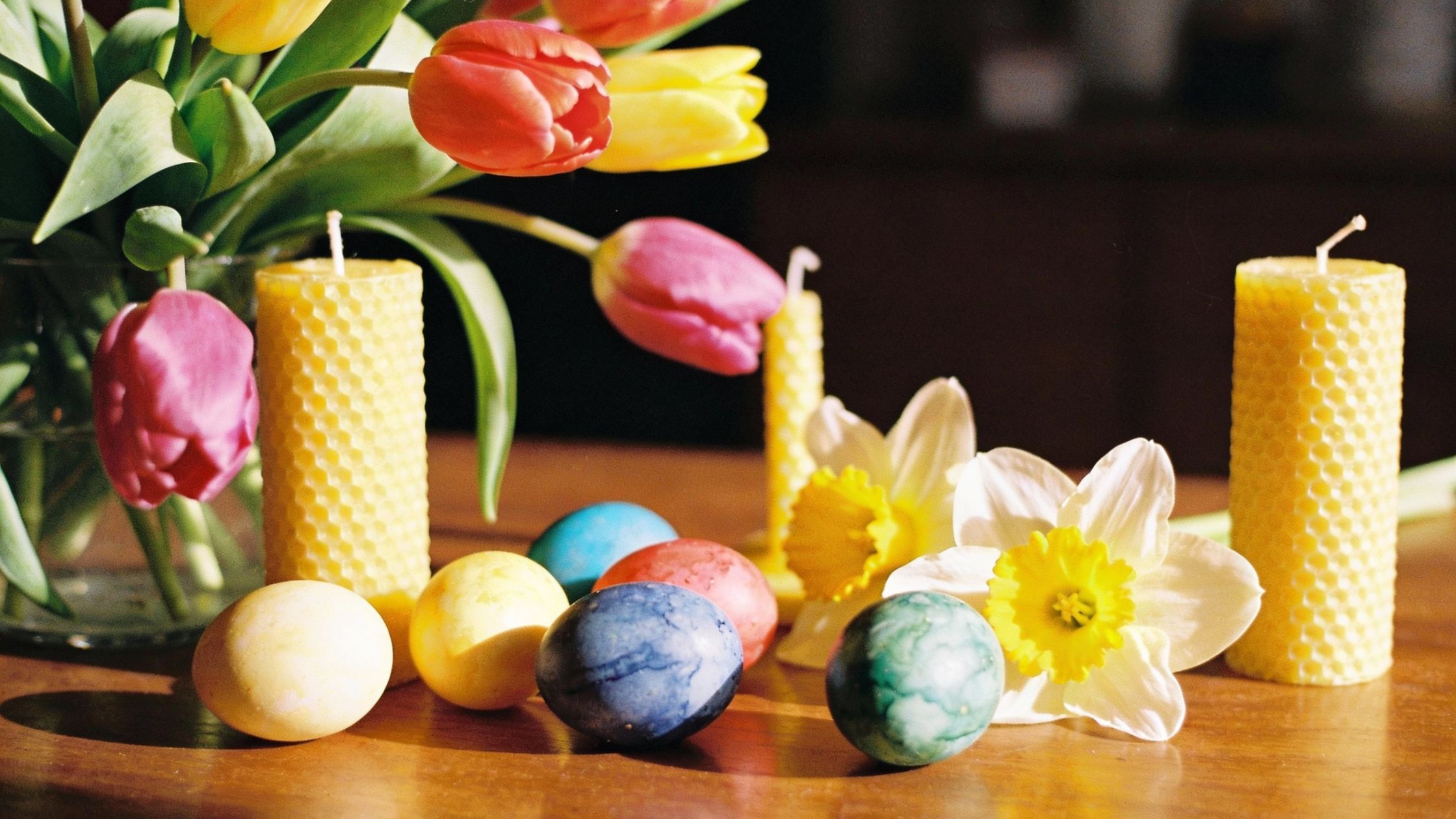 1 Fruehlingsblumen gefaerbte Eier gelbe Kerzen auf Tisch