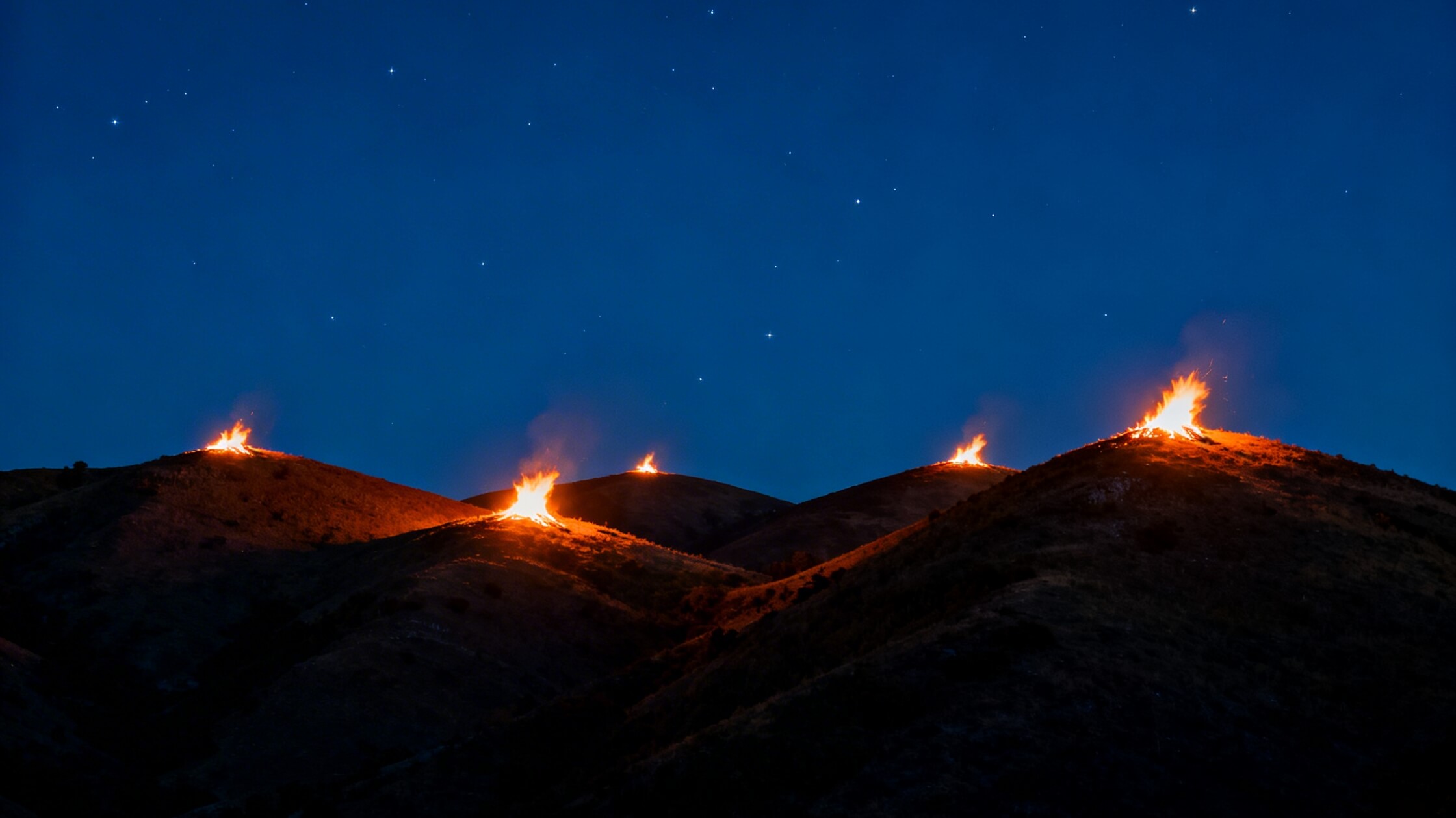 Mehrere Johannisfeuer auf Huegelkuppen in der Sommersonnenwende-Nacht - das traditionelle Litha-Ritual der brennenden Anhoehen