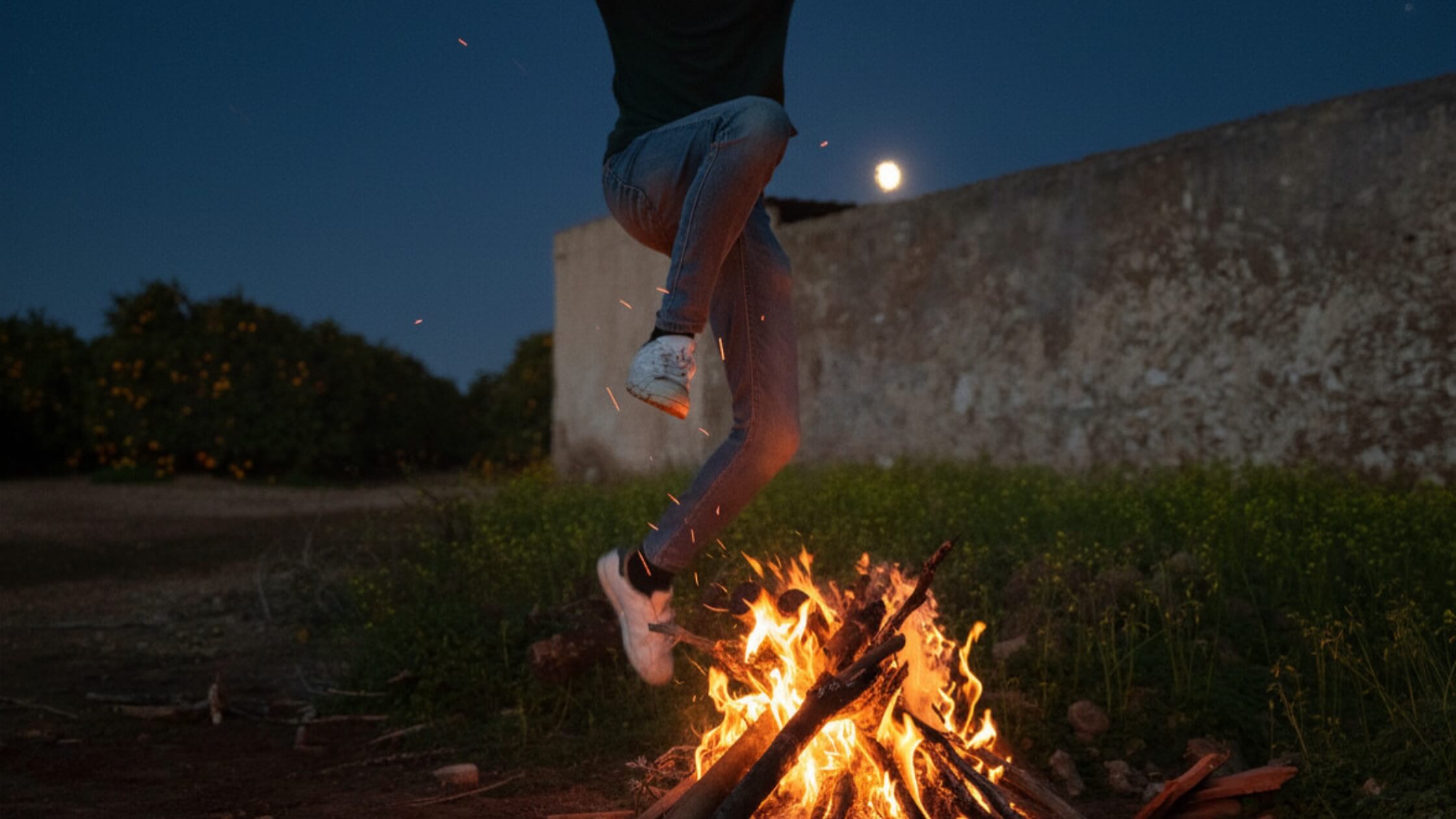 Person springt über Beltane-Feuer 2026, traditionelles Fruchtbarkeitsritual bei Walpurgisnacht, mutiger Sprung über Flammen zum Maifest